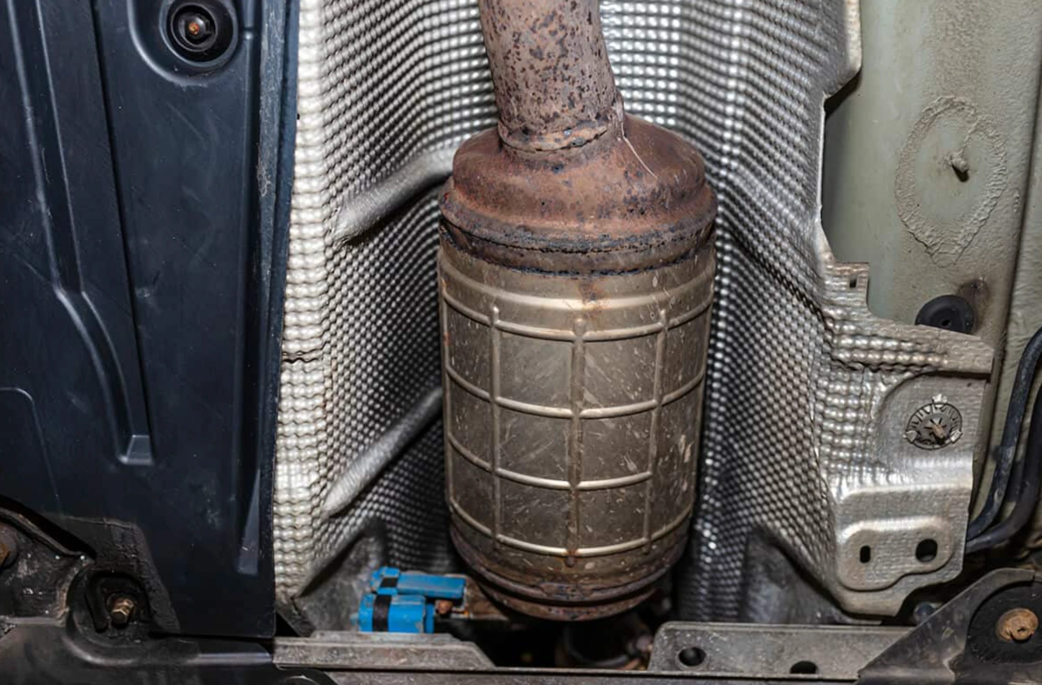 Rusty exhaust pipe and muffler in a vehicle's engine bay with a heat shield nearby. Як видаляти екологію у дизельних автомобілях правильно?