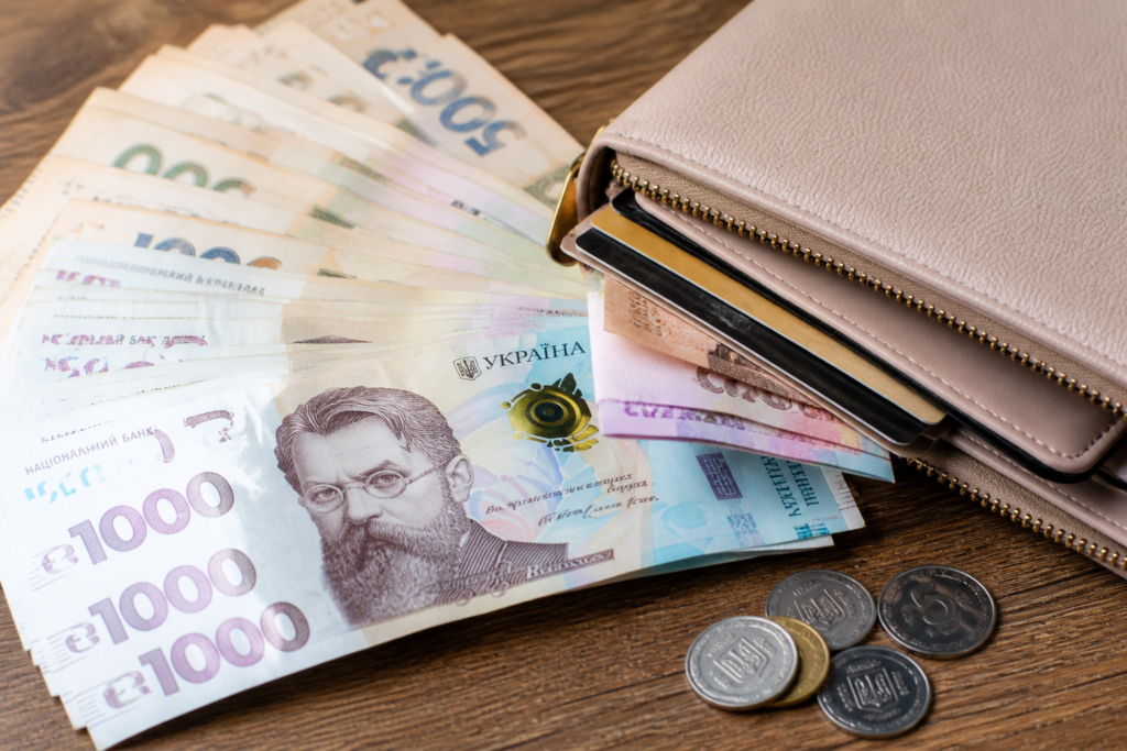 Pink wallet with Ukrainian hryvnia banknotes and coins on a wooden surface