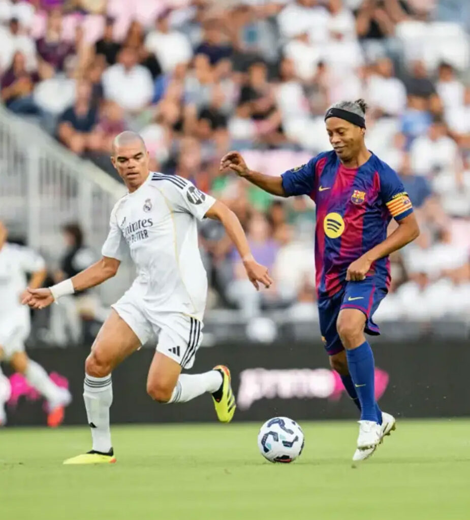 Real Madrid and Barcelona players chase the soccer ball during a match, with a crowded stands in the background. Легенди Барселони і Реала зіграли в Майамі