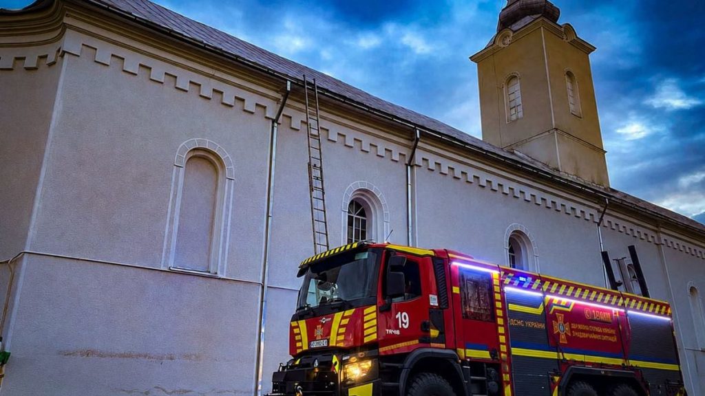 Символічна сцена з пошкодженим вівтарем, погашеною свічкою і захисним шоломом, без людей