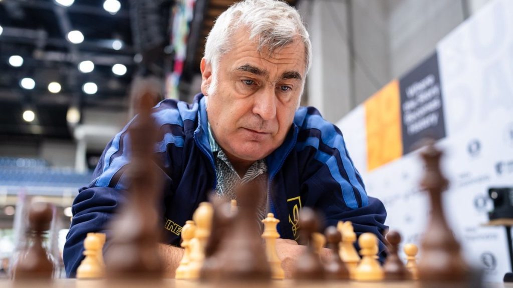 Шахова дошка з фігурами та почесною табличкою на тлі м'якого світла, поряд – український прапор