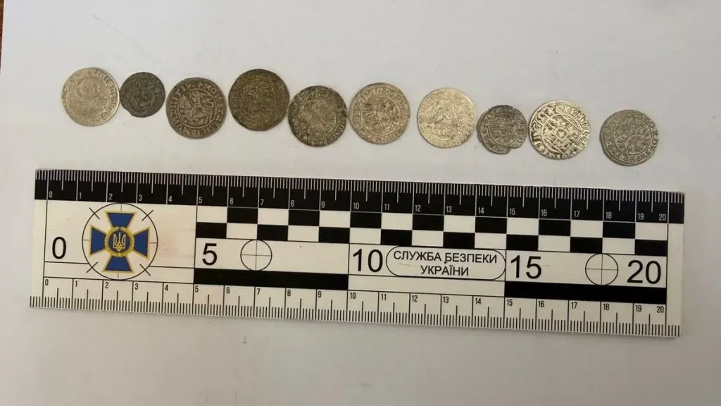 Старовинні монети та зіп‑пакети на деревʼяному столі поруч із валізою