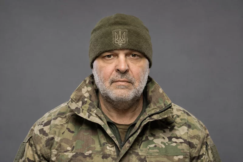 згорнута військова форма, каска і свічка на дерев'яному столі, приглушені кольори