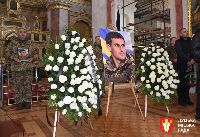 білявтрачений футбольний бутс поруч із військовим жетоном і складеним прапором України на дерев'яному тлі
