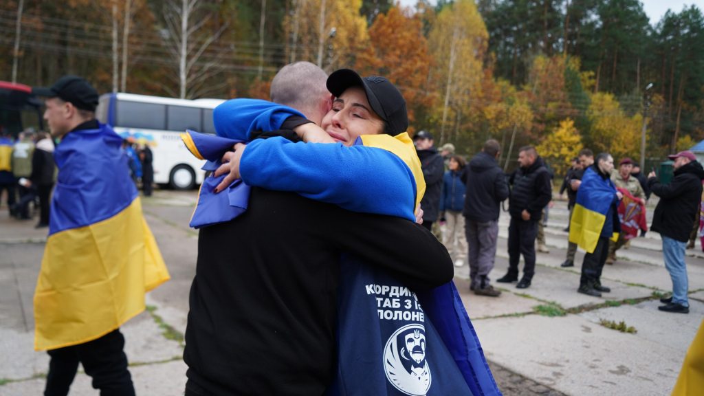 символічна сцена із складеним прапором України, військовим жетоном і квітами на дерев'яному столі