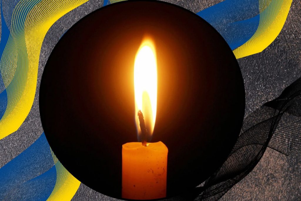 військові черевики, запалена свічка і колос пшениці на темному тлі