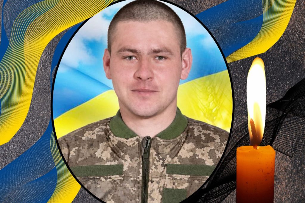 згорнутий шолом і жетон на деревʼяному столі з стрічкою прапора України