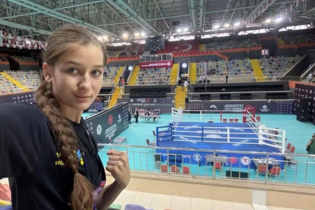 Боксерські рукавички молодіжного розміру на підлозі спортзалу поруч зі складеним українським прапором