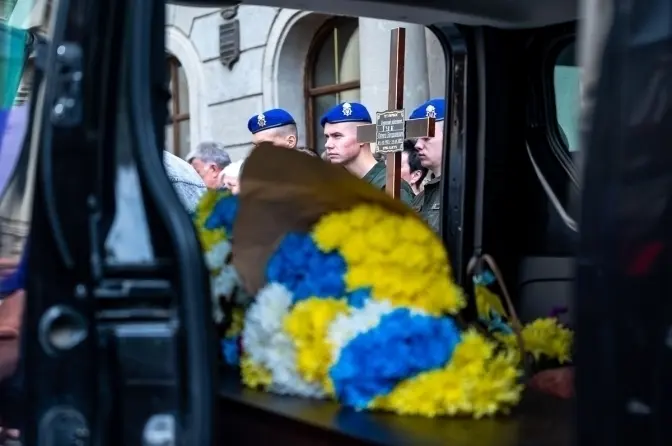 символічна натюрмортна сцена: два складені військові кашкети, букет з пшениці і волошок на дерев'яному столі, м'яке світло, розмитий інтер'єр церкви, без облич і тексту