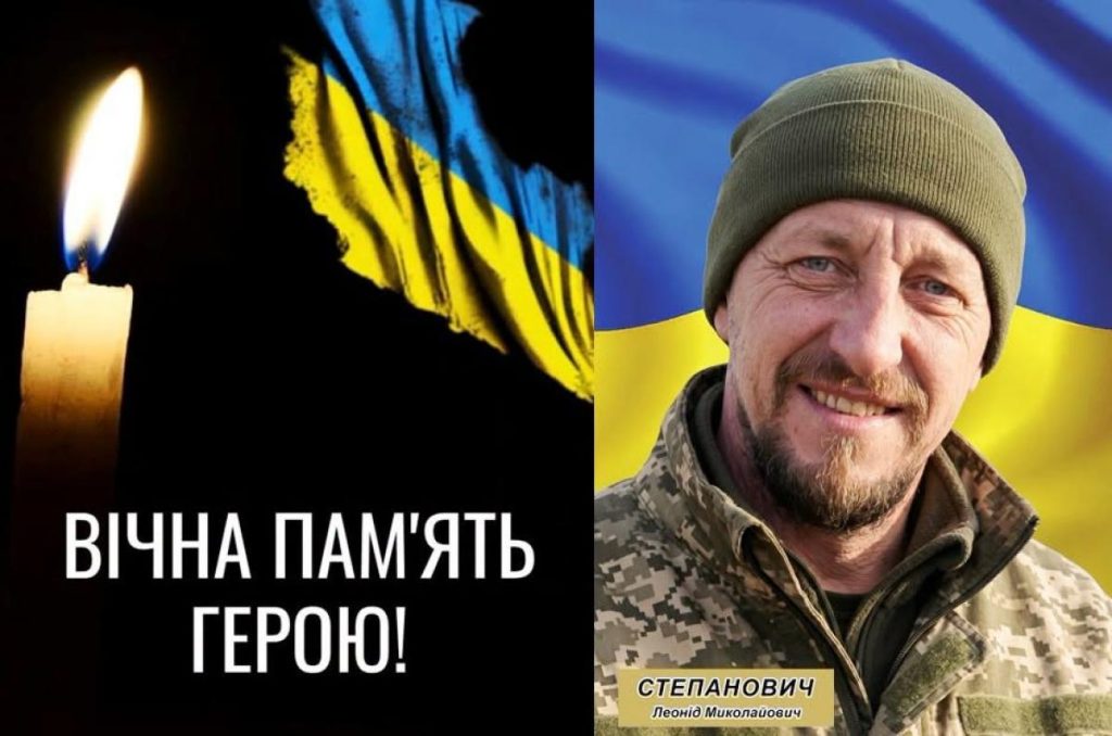 скромна похоронна композиція: складений військовий кашкет, свічка і прапор України на столі