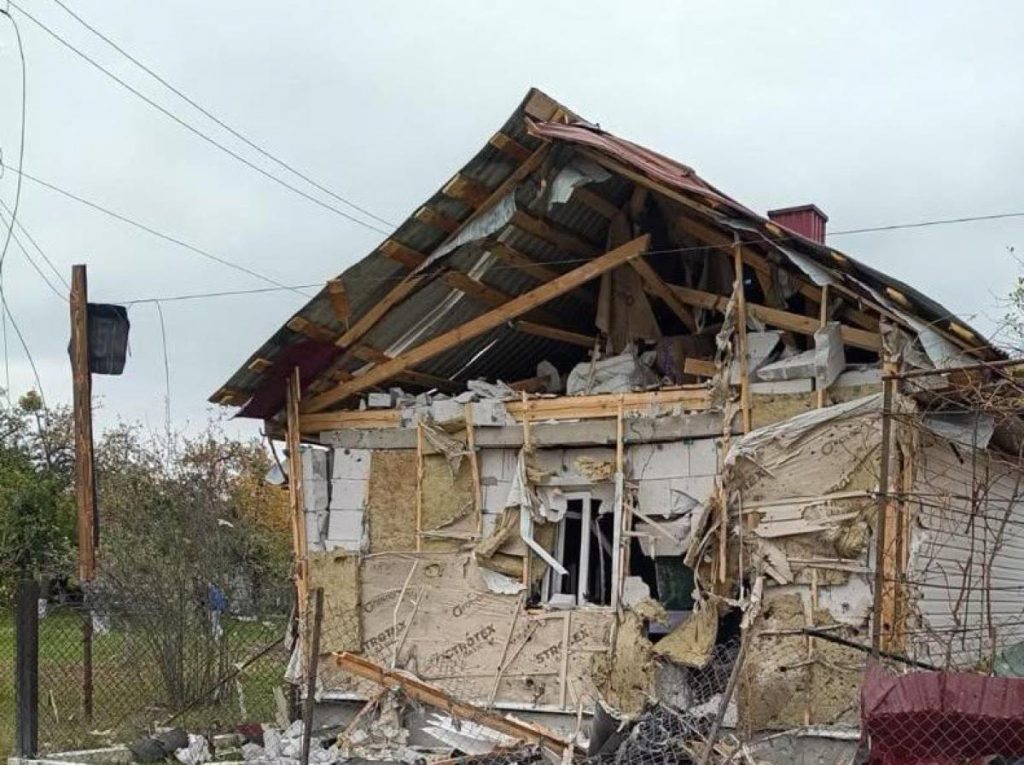 Пошкоджений будинок, уламки біля фасаду, темне небо та віддалений світло маячків служб