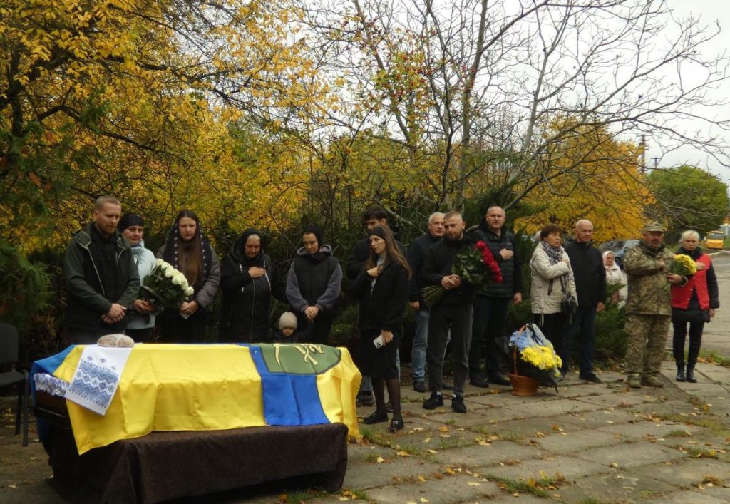 Символічна сцена: складена форма і шолом на лавці зі свічкою та вінком