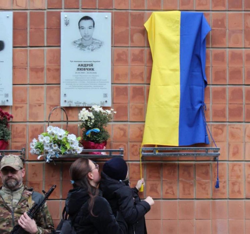 крупний план бронзової меморіальної дошки на стіні з букетом польових квітів і стрічкою