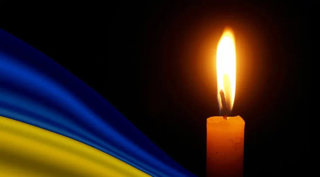 Крупний план запаленої свічки поруч із військовим нарукавним знаком на темній поверхні, траурна атмосфера