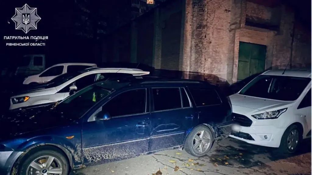 Два припарковані автомобілі з ушкодженнями вночі під вуличним ліхтарем, відблиски поліцейських маячків