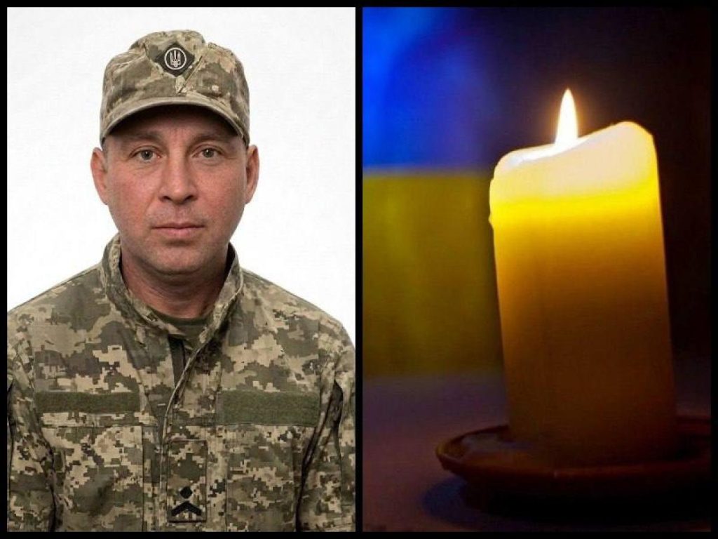 Військовий шолом і складений мундир поруч зі свічкою та прапорцем на дерев'яному столі