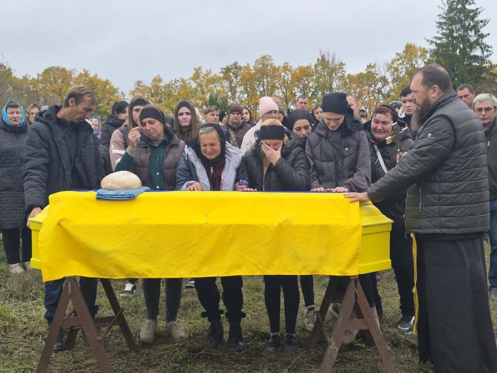 складений військовий прапор із шоломом і черевиками на столі, свічка і квіти