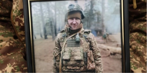 символічна композиція зі складеним військовим шарфом, книгою й запаленою свічкою