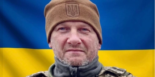 символічна композиція: свічка, жетон і маленький прапор України на дерев'яній поверхні