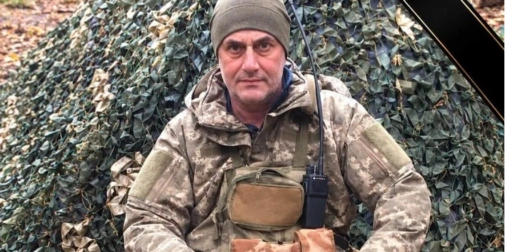 Крупний план: футбольна бутса поруч зі складеним прапором України і запаленою свічкою на траві
