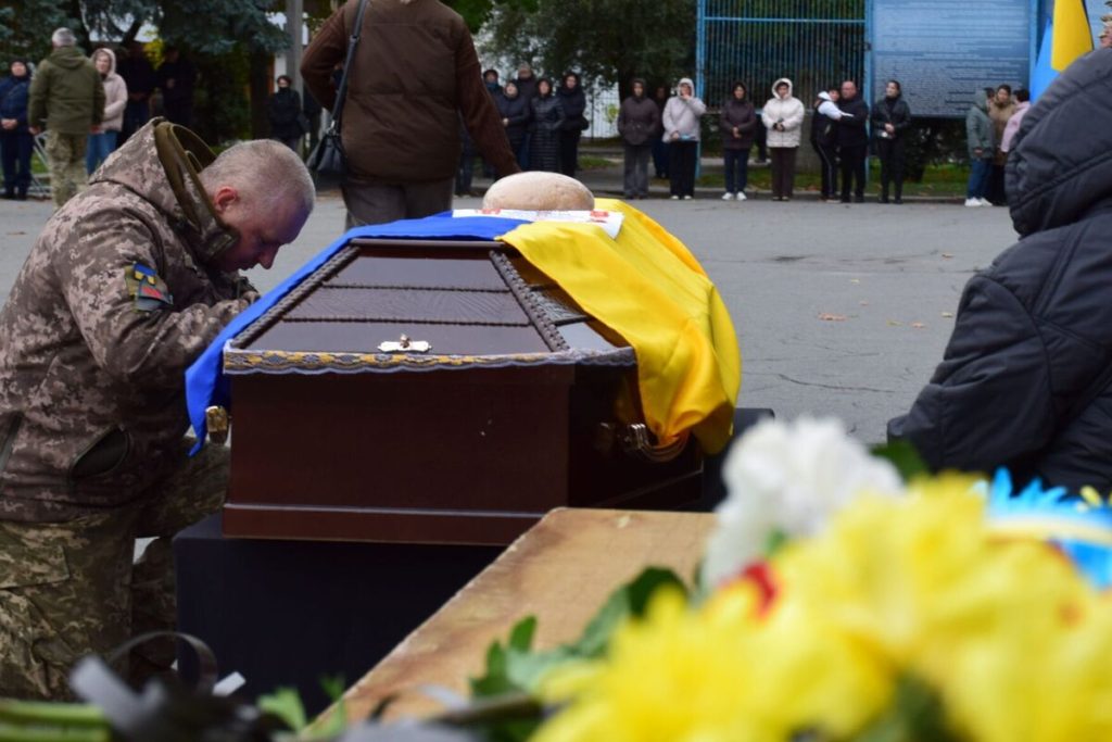 згорнутий військовий кітель, шолом і запалена свічка на дерев'яному столі