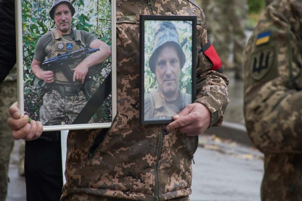 Берці з жетонами та запалена свічка на тлі тканини синьо-жовтих кольорів